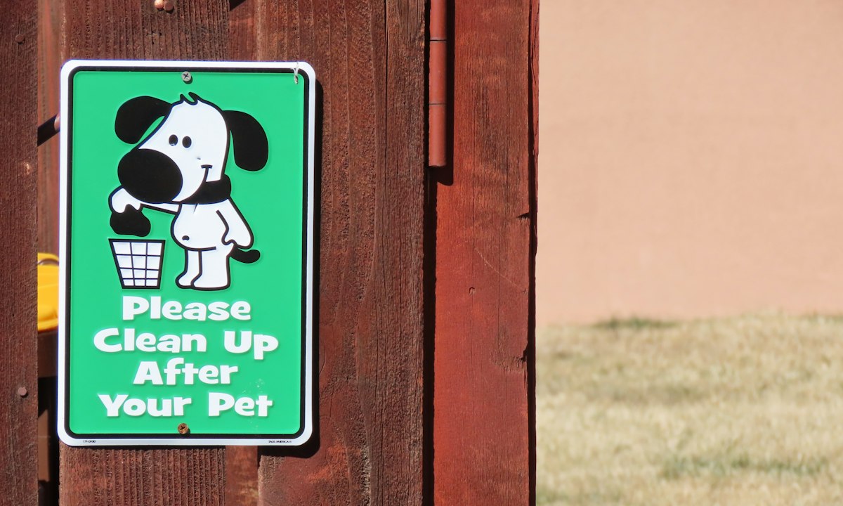 "Please Clean Up After Your Pet" sign on a wooden fence – a reminder about dog poop cleanup and pet waste removal